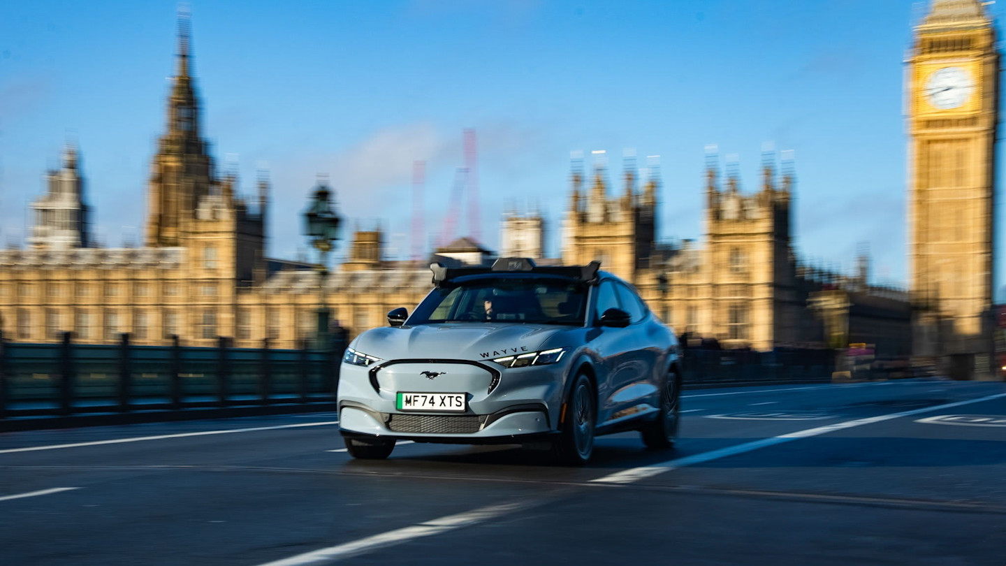 A Wayve self-driving car with sensors mounted on the roof drives past the UK Houses of Parliament and Big Ben in London.