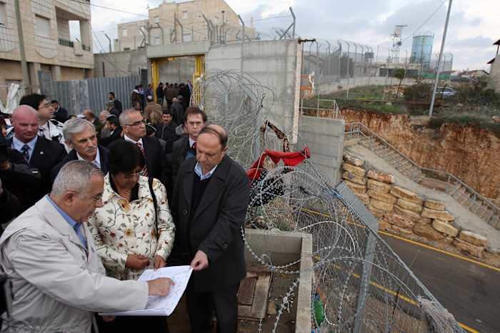 Navi Pillay and Salam Fayyad examine a map with others near barbed wire and a concrete barrier in a West Bank settlement.