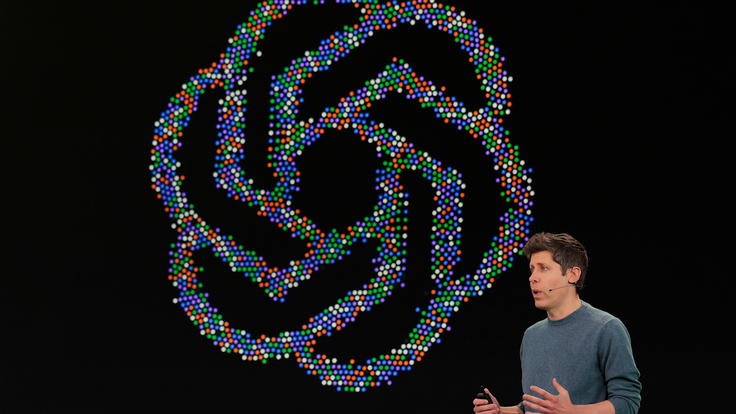 Sam Altman speaks on stage in front of a large OpenAI logo made of colorful dots during the OpenAI developers conference.
