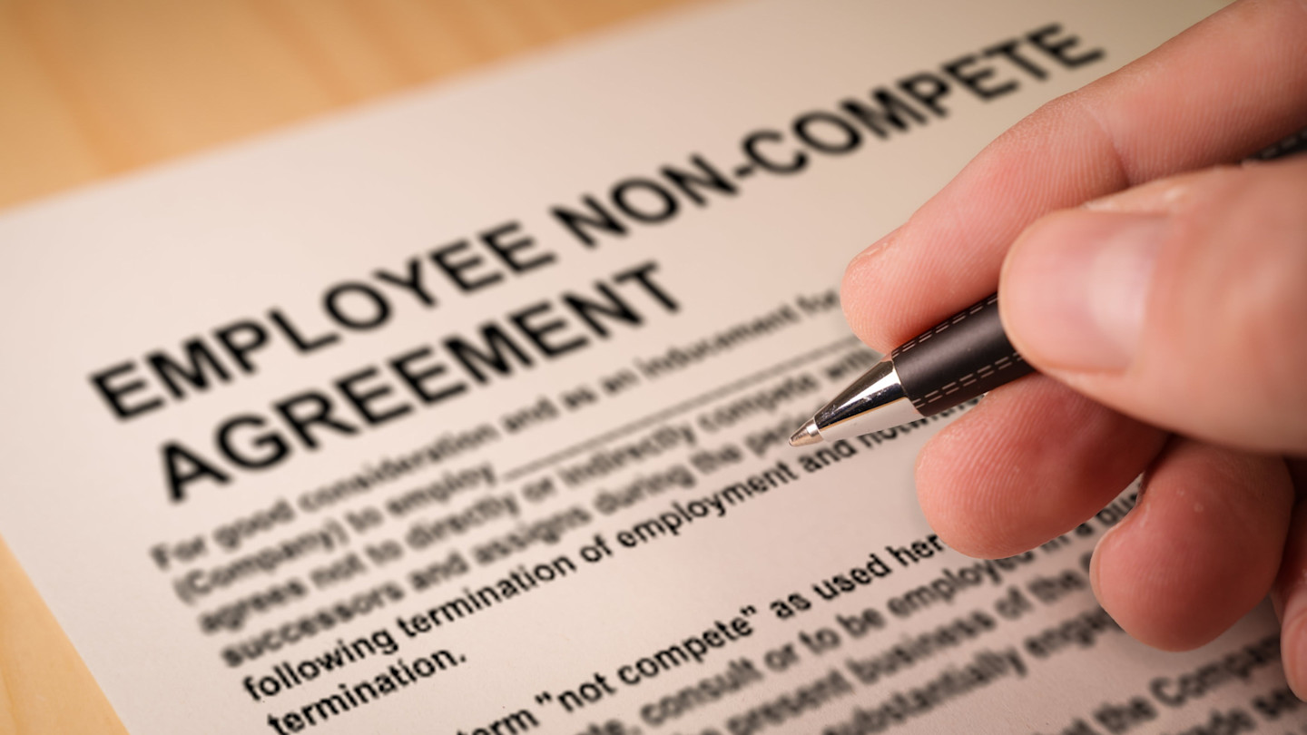 A person holding a pen prepares to sign an employee non-compete agreement document.