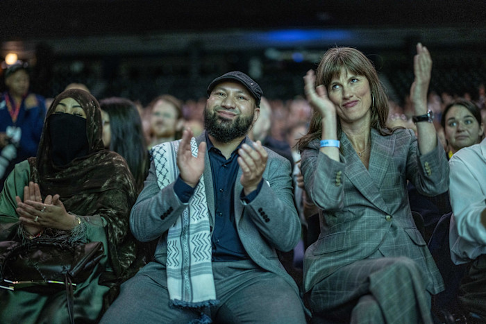 Mothin Ali and Rachel Millward sit side by side, clapping among other attendees at a Green Party conference.
