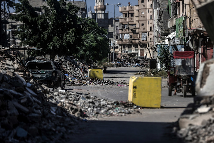 Yellow concrete blocks divide a street lined with rubble and damaged buildings in Gaza City’s Sanfura junction.