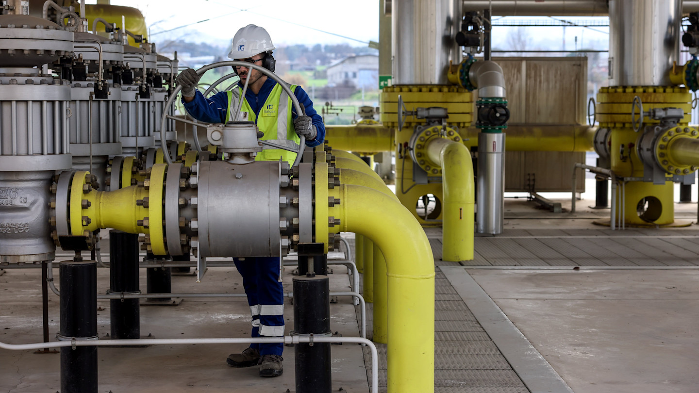 A worker wearing safety gear inspects a large valve meter surrounded by yellow pipes at the Pantano reduction station operated by Italgas SpA.