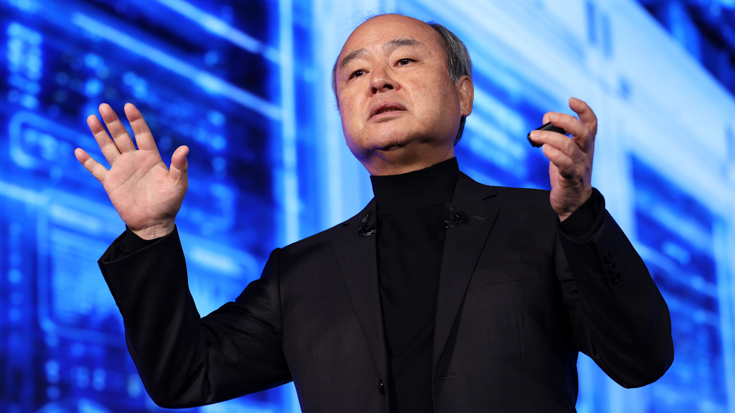 Masayoshi Son gestures with both hands while speaking on stage at the SoftBank World forum, with a blue digital background behind him