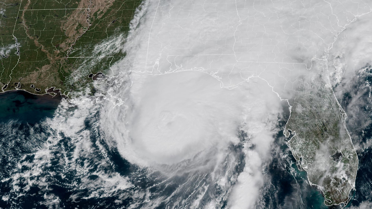 A satellite image shows Hurricane Isaias with a defined eye approaching the Gulf Coast of Alabama and Florida, covered by dense clouds.