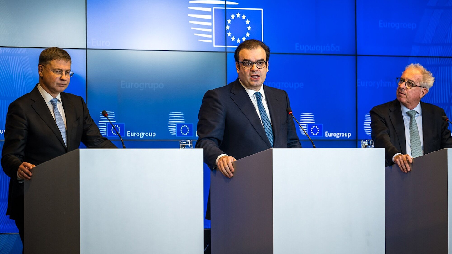 Valdis Dombrovskis (left), Kyriakos Pierrakakis and Pierre Gramegna speak at podiums during a Eurogroup news conference.