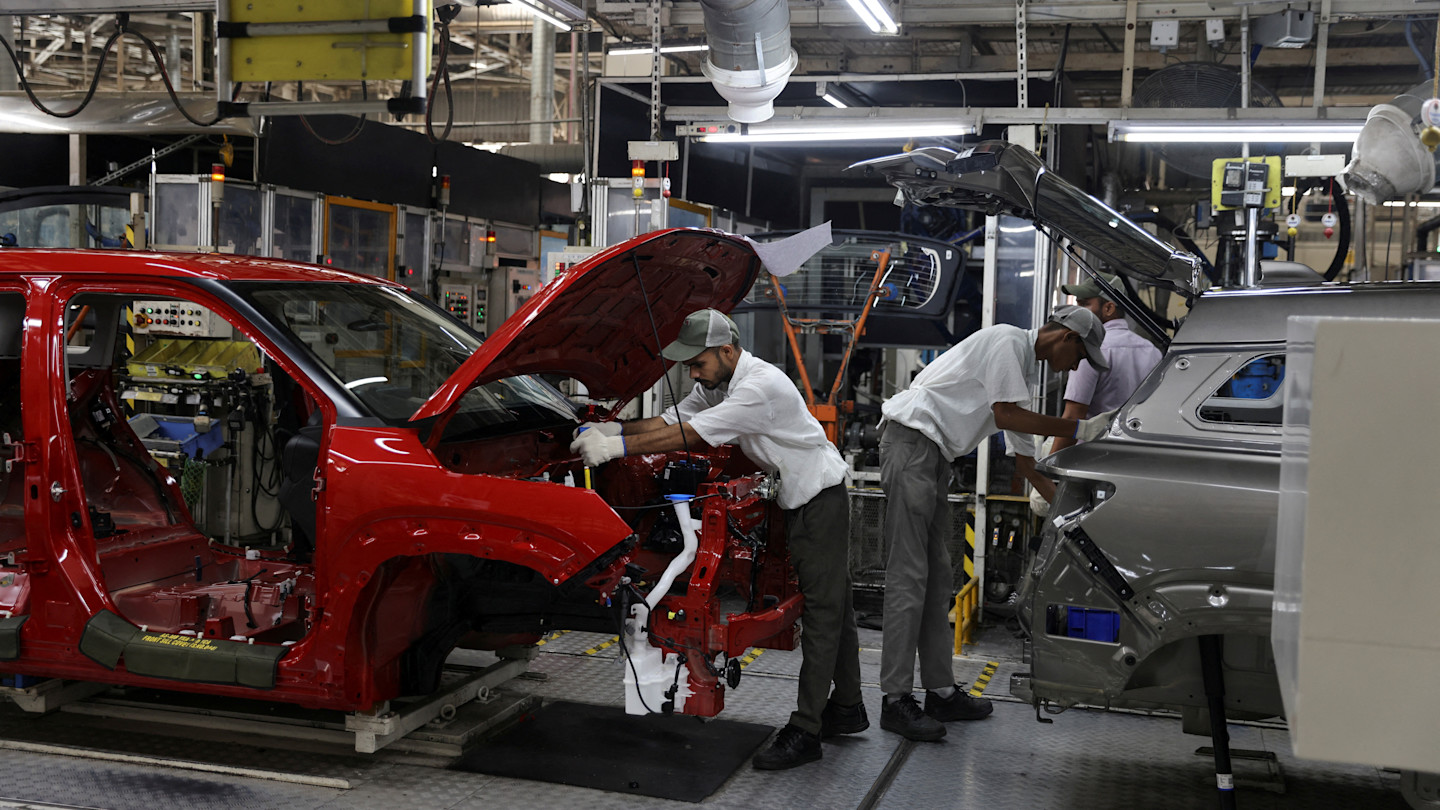 Employees assemble different parts on to a car panel at the manufacturing plant of Maruti Suzuki