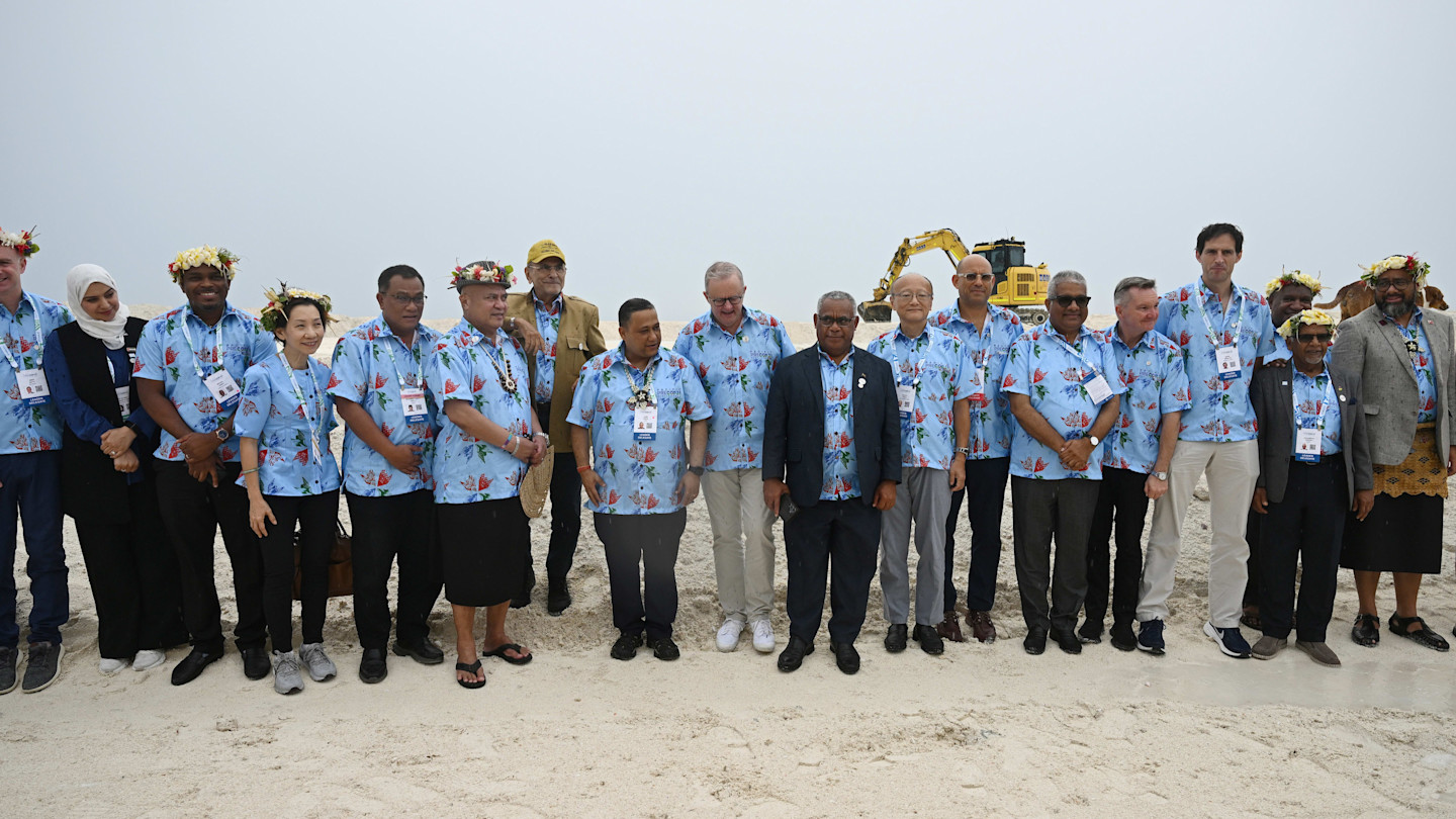 Anthony Albanese stands with Pacific island leaders at a land reclamation site, all wearing blue floral shirts and name badges.