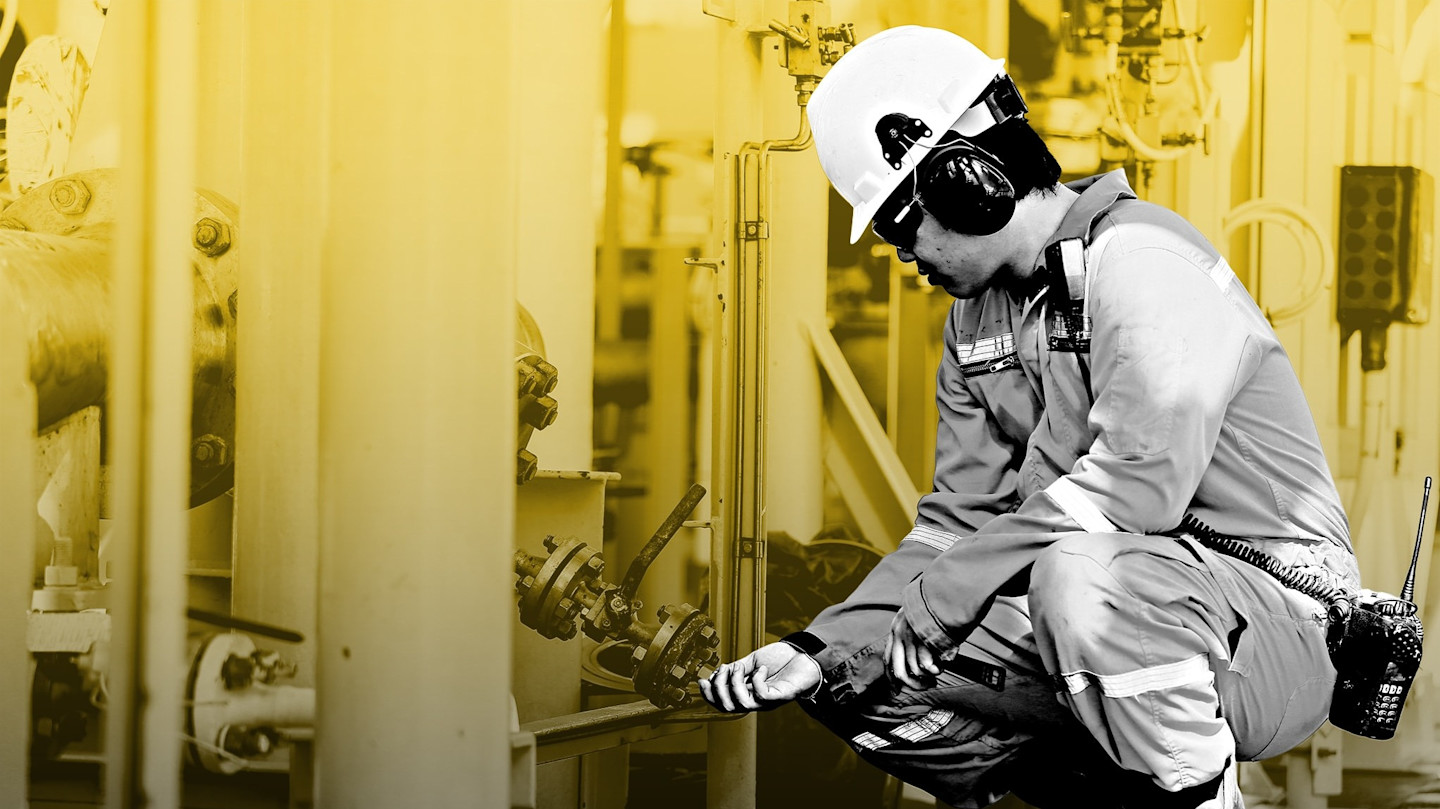 A worker in safety gear, including a hard hat and ear protection, inspects equipment at an offshore oil and gas facility.