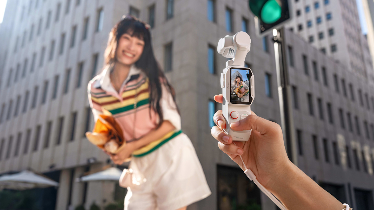 A person holds an Insta360 Luna Pro camera, which displays a screen showing a smiling woman posing outdoors in front of city buildings.