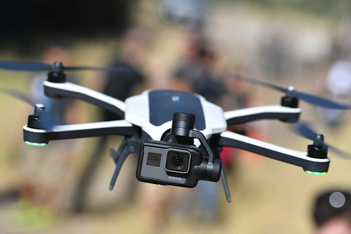 A GoPro Karma foldable drone with camera attached flying outdoors, with blurred people in the background.