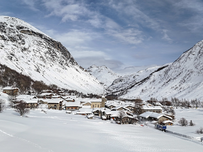 A snow-covered alpine village surrounded by mountains beneath a cloudy sky.