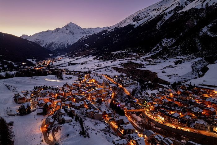 A village with its lights on, surrounded by snow and mountains