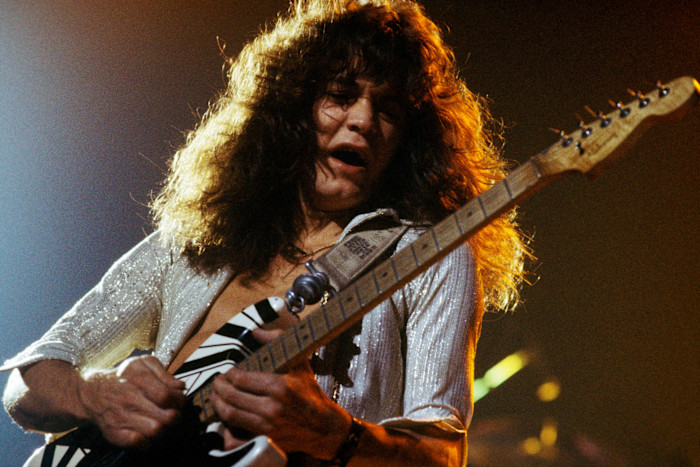Eddie Van Halen performing onstage with a striped electric guitar at the Rainbow Theatre.