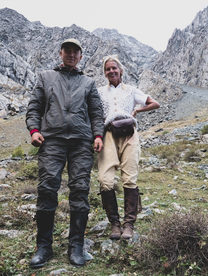 Alexandra Tolstoy stands next to a herder in outdoor clothing, with rocky mountains in the background.