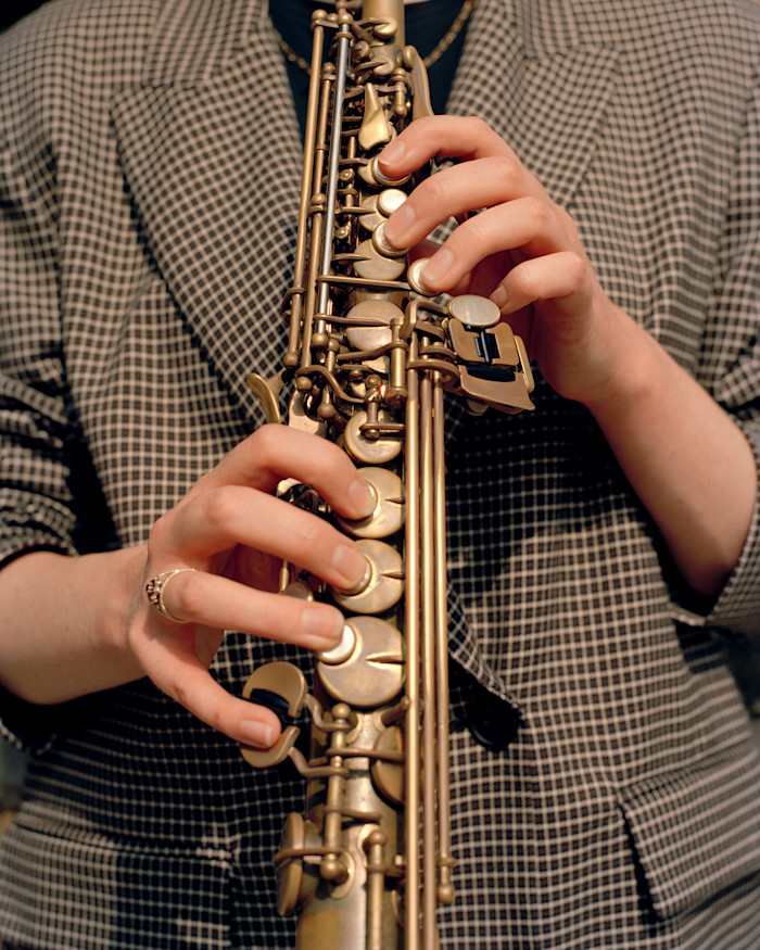 Jess Gillam’s hands playing a saxophone, wearing a checkered jacket.