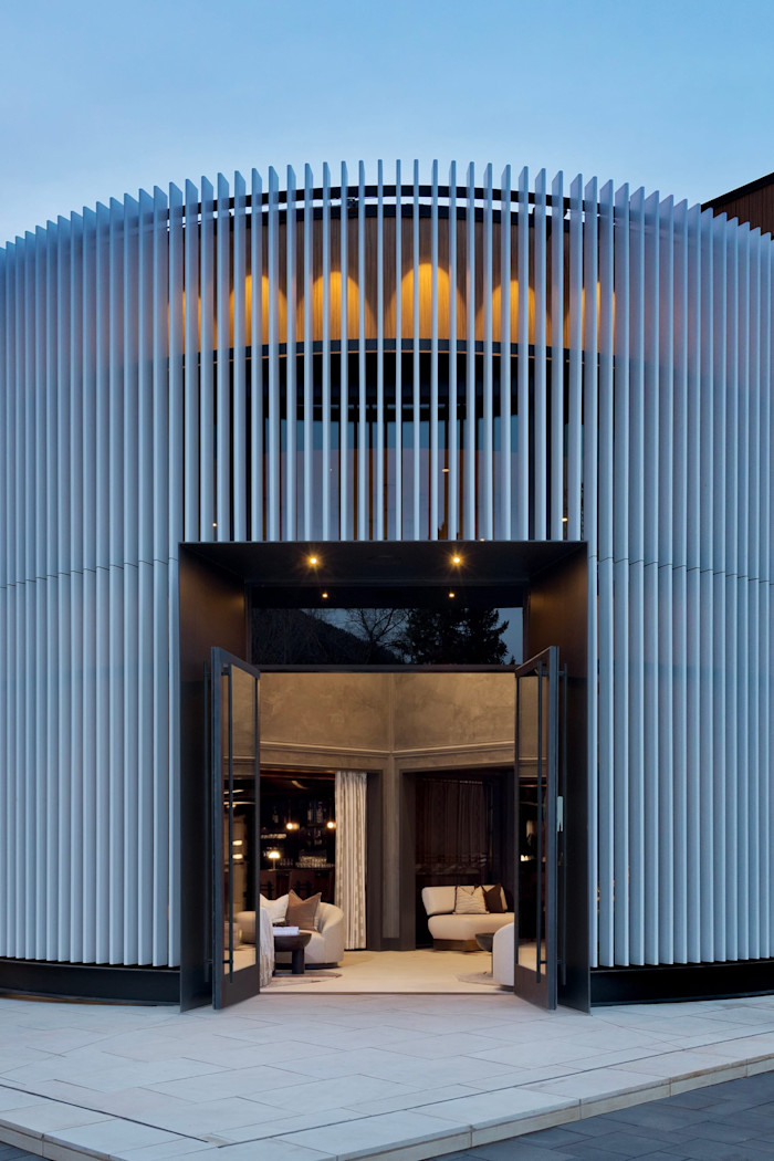 The exterior of the White Elephant features a modern, curved facade with vertical white fins and large glass doors opening to a stylishly furnished interior