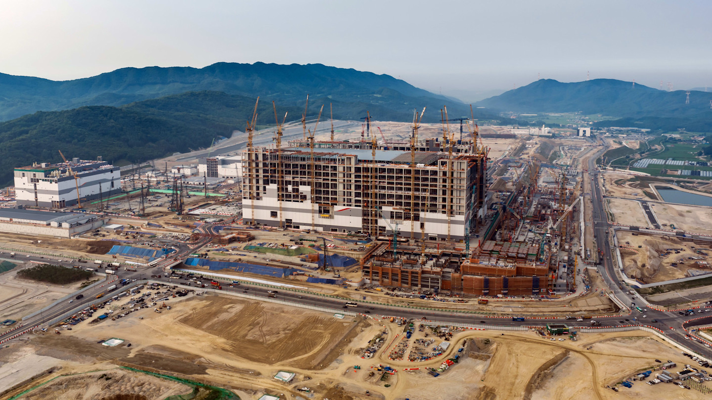 SK Hynix semiconductor plant under construction, with cranes surrounding a large unfinished building and mountains in the background.