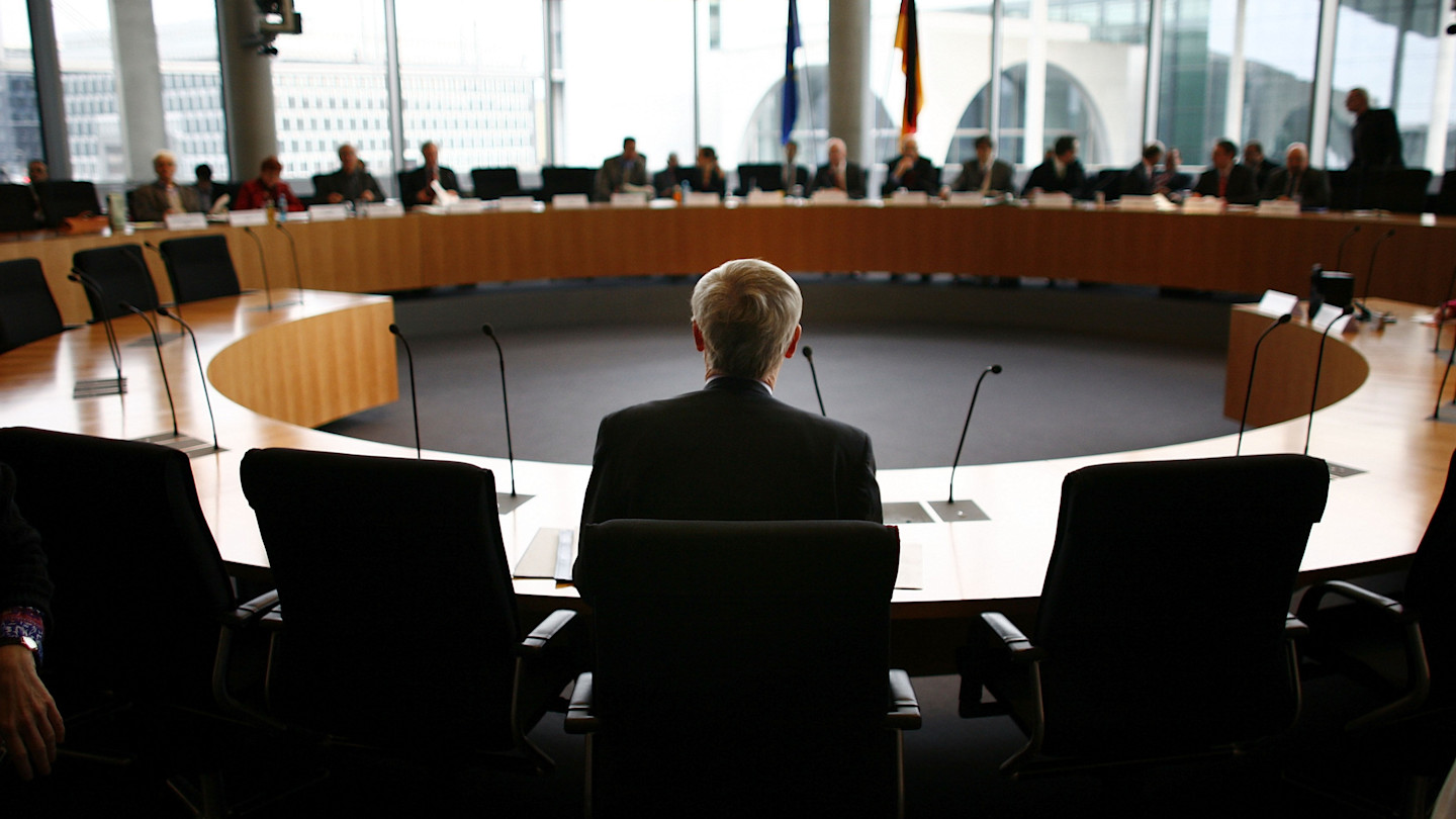 August Hanning sits at a curved table facing a Bundestag committee during a hearing, with microphones in front of him.