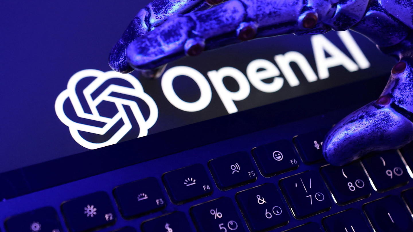 An illustration showing a robotic hand above a keyboard with the OpenAI logo and name displayed in the background.