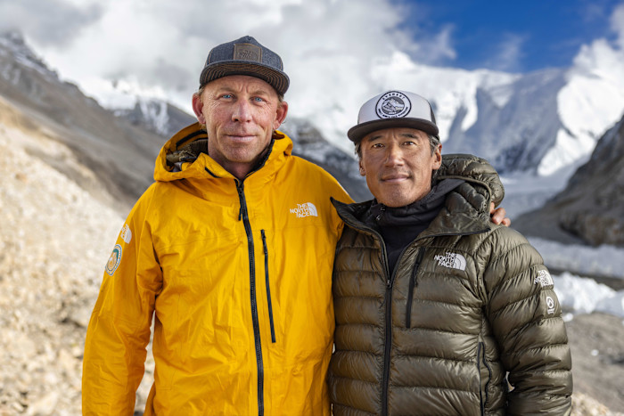 Jim Morrison, left, and Jimmy Chin stand outdoors in winter jackets with snowy mountains in the background.