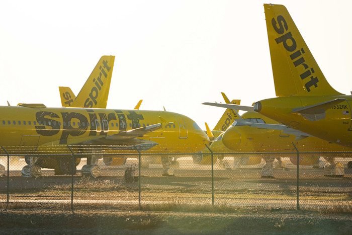 Several Spirit Airlines planes painted bright yellow are parked behind a fence at Phoenix Goodyear airport.
