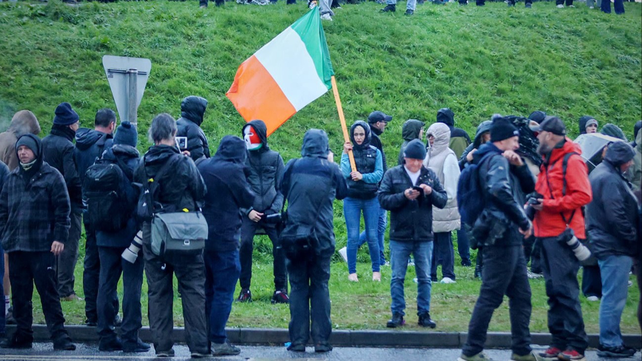 A group of protesters, some with cameras, block a road in Portadown as a woman holds an Irish flag during the Drumcree dispute.