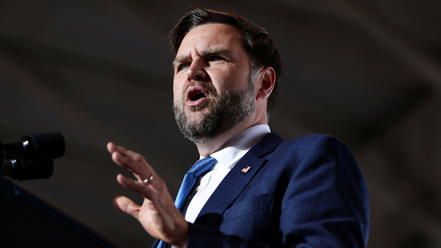 JD Vance speaks at a rally, gesturing with his hand and appearing to address the audience emphatically.