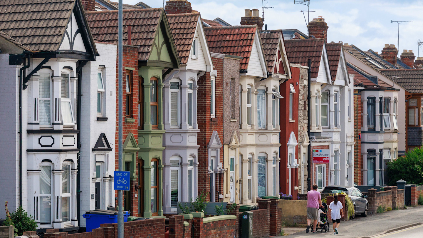 A row of colourful terraced houses in Portsmouth with a man, woman and child walking on the pavement in front.