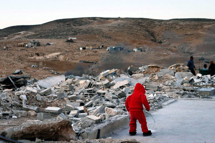 A lone child in a red hoodie and back to the camera, wandering amid a scene of devastation and rubble.