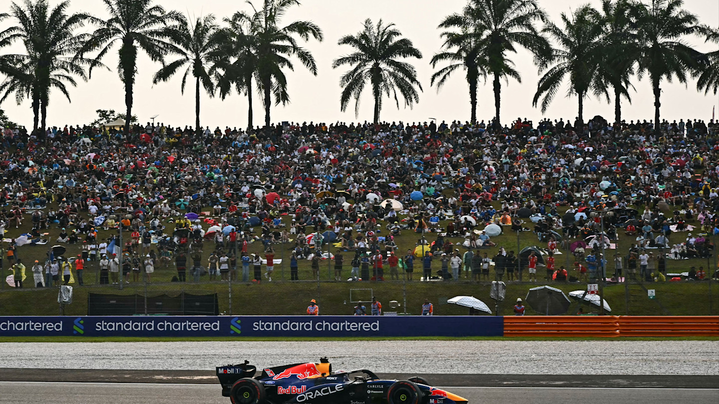 Max Verstappen drives his Red Bull Racing car past a large crowd of spectators and palm trees during the Formula One Bahrain Grand Prix.