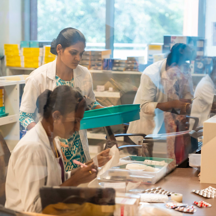 Four pharmacists in white lab coats prepare and organise medication behind a counter.