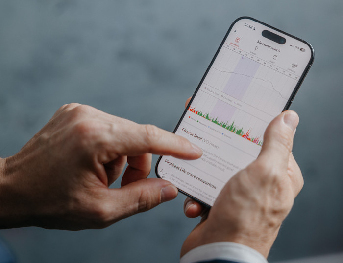 A person uses a smartphone displaying health monitoring data, including stress, sleep, exercise and fitness measurements.