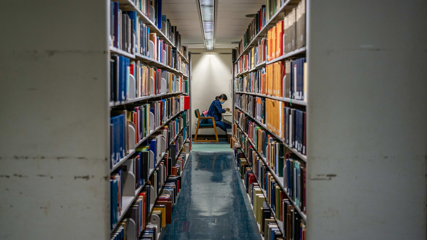 A person sits alone reading at a desk between tall bookshelves in the Rice University Library in Houston, Texas.
