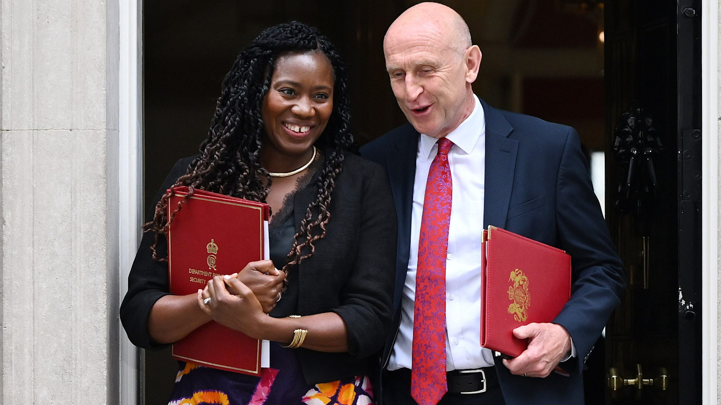 Miatta Fahnbulleh and John Healey smiling as they leave 10 Downing Street, each holding a red government folder.