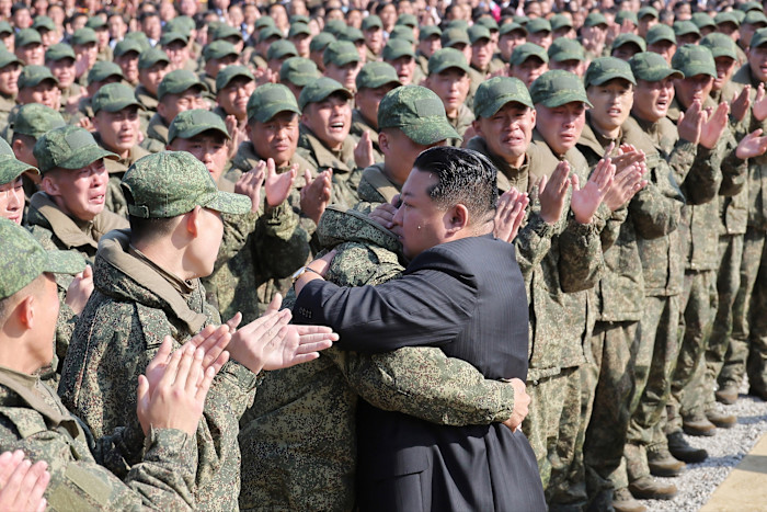 Kim Jong-un embraces a soldier in camouflage uniform as rows of soldiers clap