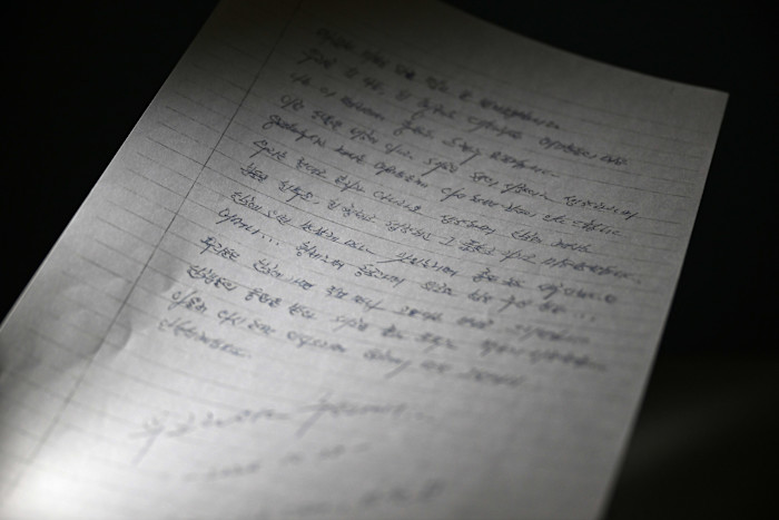 A letter written in Korean on lined paper, with the text slightly blurred and slanted under a direct light.