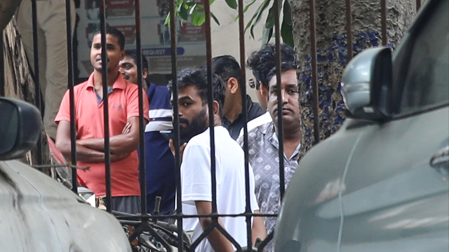Abhijeet Dipke stands among several men behind a metal fence outside a court building in New Delhi