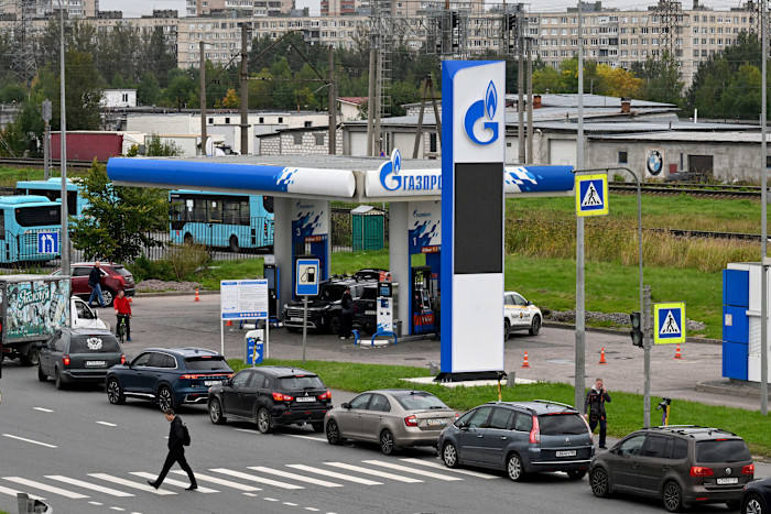 Several cars are lined up at a Gazprom petrol station in Saint Petersburg, with people walking and waiting nearby.