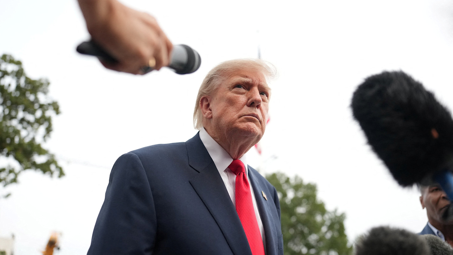 Donald Trump speaks to reporters outdoors, with several microphones held out toward him.