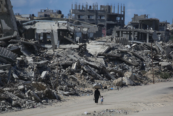 A Palestinian woman and child walk past destroyed buildings in the Jabalia refugee camp on October 5 2026