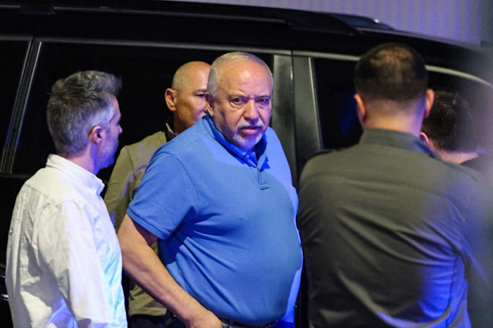 Avigdor Liberman, wearing a blue shirt, stands among several people outside near a vehicle at night