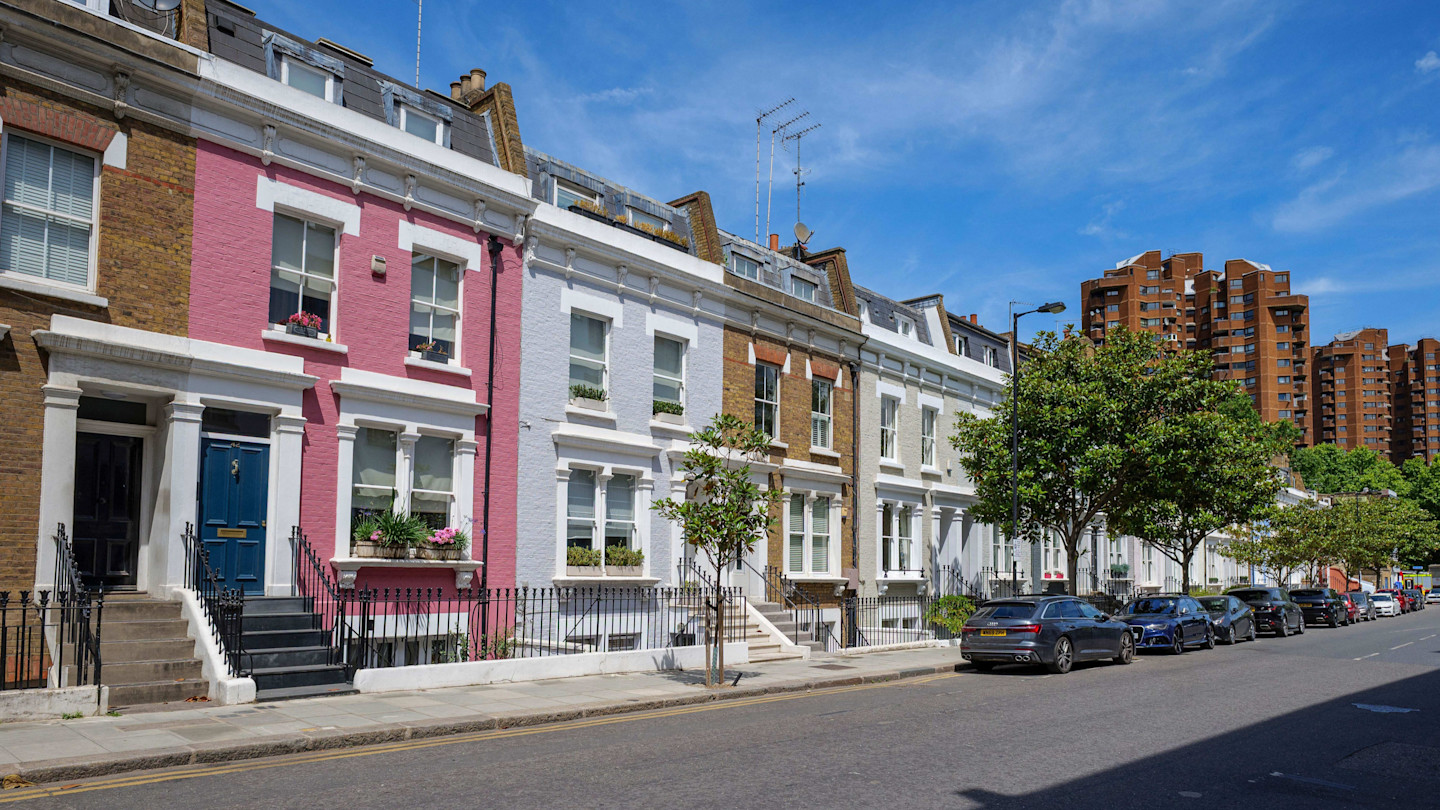 Row of colourful terraced houses on Lots Road with parked cars and brown apartment buildings in the background.