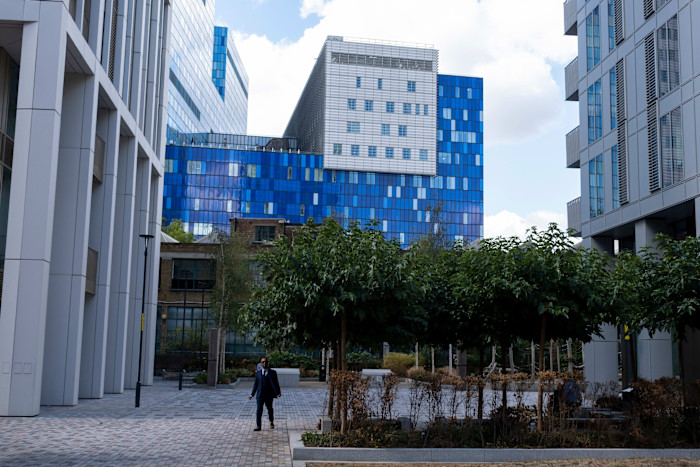 Blue glass exterior of the Royal London Hospital’s modern building, with a person walking in the foreground among trees and courtyard.