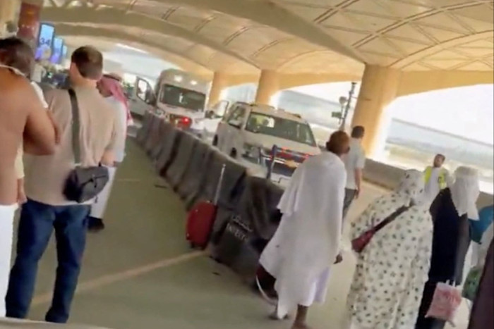 Ambulances parked outside an airport terminal as several people walk nearby, some carrying luggage.