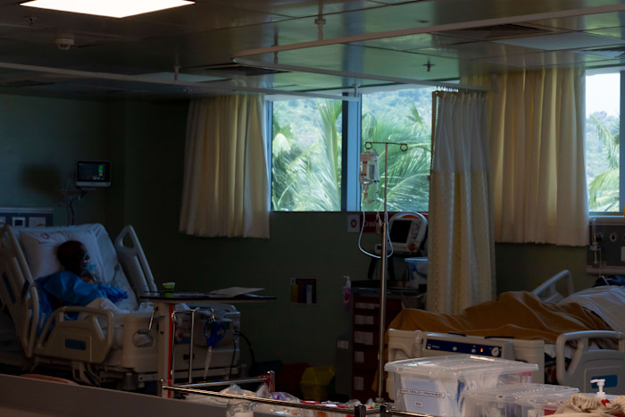 A patient wearing an oxygen mask lies in a hospital bed in a dimly lit room at KIMS Health Nagercoil.