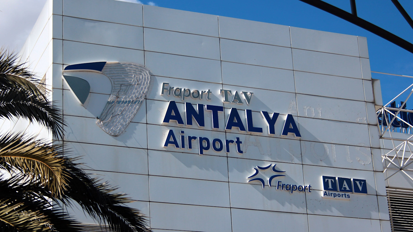 Sign for Fraport TAV Antalya Airport on the exterior wall of the terminal, with logos and palm leaves visible.