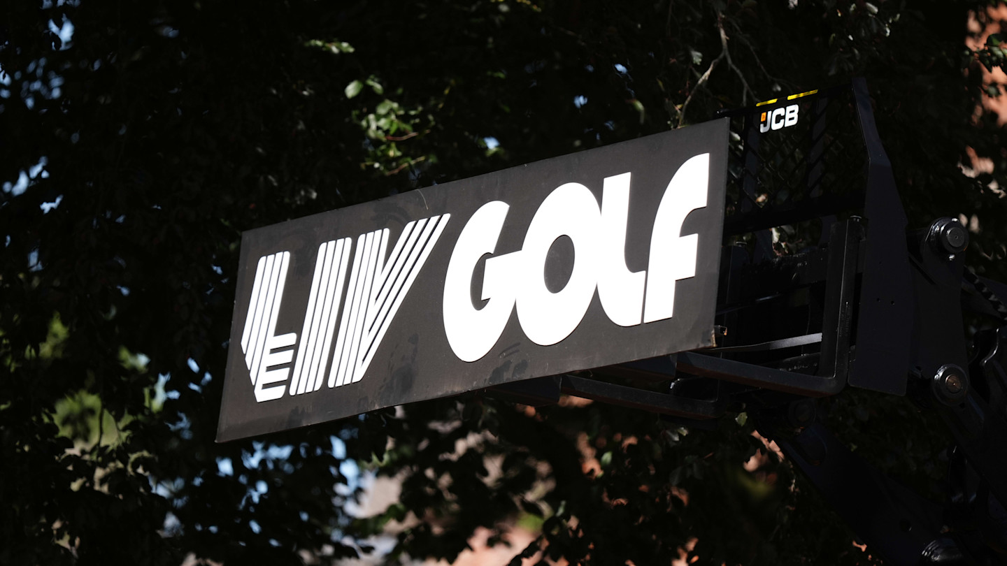 Close-up of the LIV Golf logo on a black sign, with trees in the background.