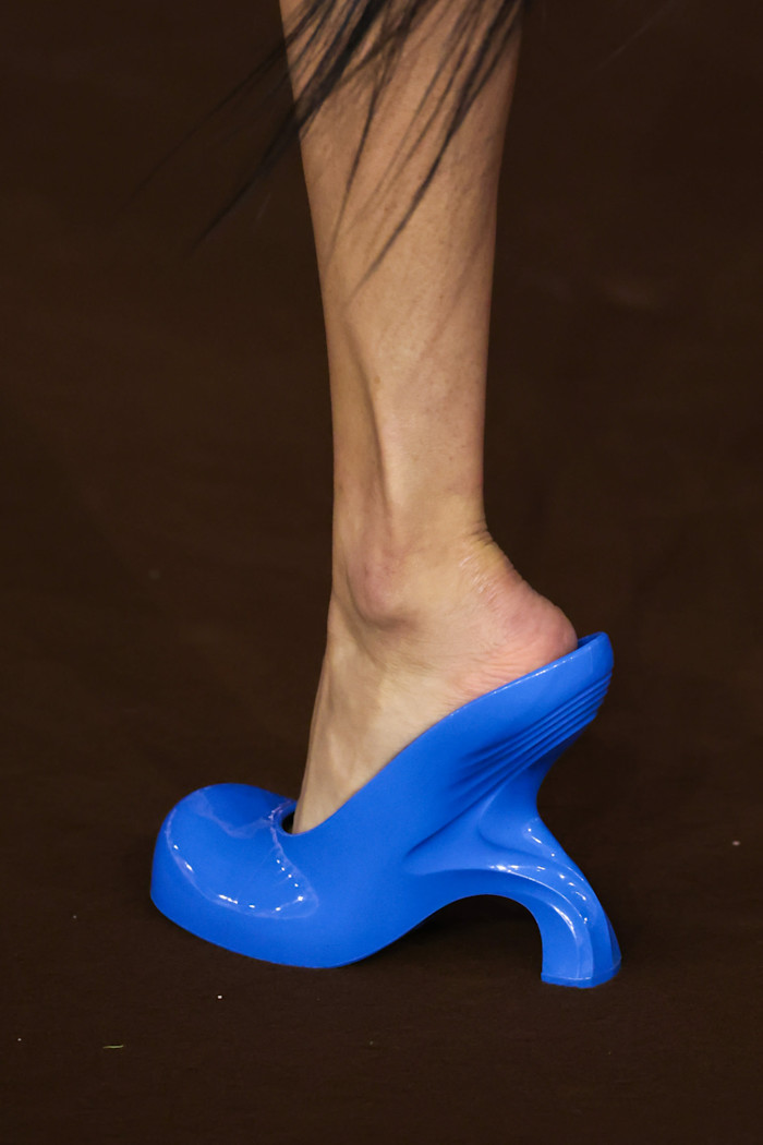 Close-up of a model’s foot wearing a sculptural, bright blue high-heeled shoe on the runway.