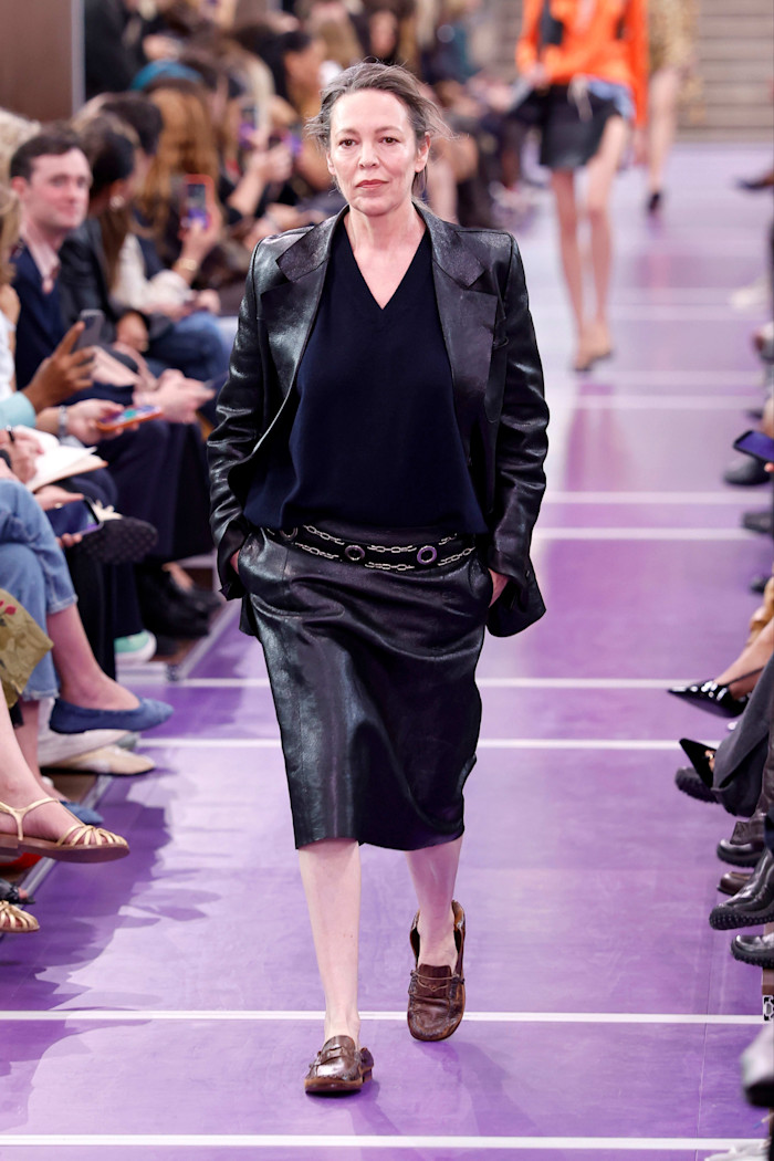 Olivia Colman walks the runway in a black leather jacket and skirt and flat shoes at the Miu Miu Spring/Summer 2027 show during Paris Fashion Week.